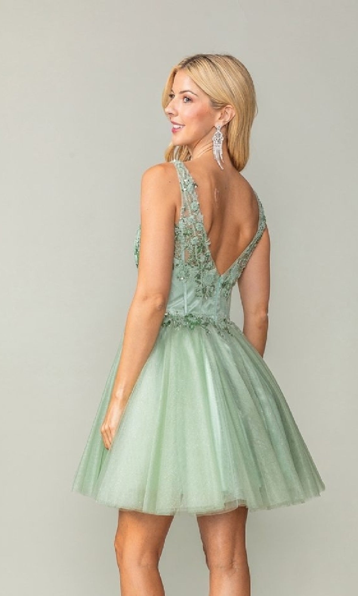 Woman wearing a light green dress with floral embellishments on a plain background